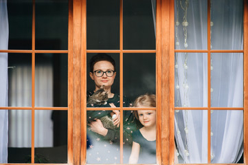 Handsome woman with pretty face hugs a beautiful daughter and looks through big window