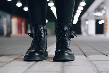 Women's feet in black shoes stand on the brick floor. A woman in the parking lot. Casual style in clothes and shoes.
