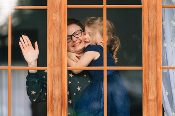 Handsome woman with pretty face hugs a beautiful daughter and looks through big window