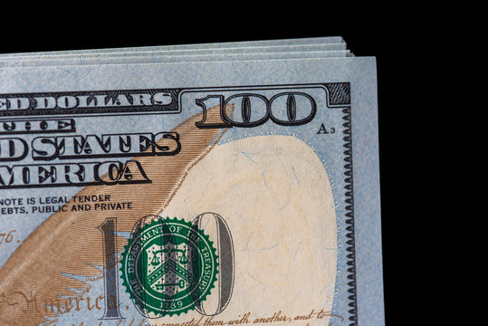 A stack of hundred dollar bills against a dark background. Photographed close-up.