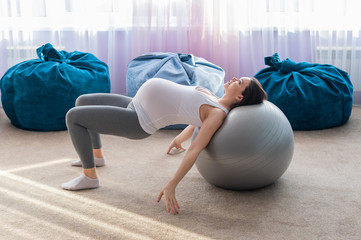 Naklejka premium Beautiful european woman doing pregnant exercises. Expectant mother is doing exercises with a fitness sword. Yoga for expectant mothers.
