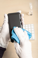 Hands with gloves cleaning mobile phone with disinfectant. COVID-19 Coronavirus outbreak contamination prevention concept