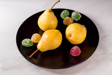 Three ripe yellow pears with sweet colorful marmalade on a black and white plate on a light background