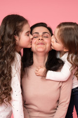 Portrait of little daughters kissing their beautiful happy mother with closed eyes
