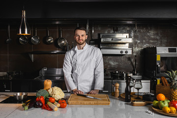 confident caucasian cook man ready to cook in kitchen, wearing white apron. professional cook make perfect garnish and other delicious dishes. look at camera. kitchen, restaurant, cook, food concept