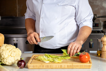 chef-cooker cut fresh vegetables on wooden board in kitchen, professional cook work in restaurant. man in apron