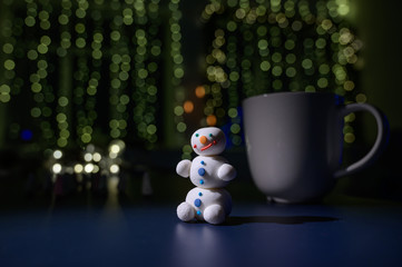 Cute snowman and little Christmas trees made of marshmallows on the background of Christmas lights....