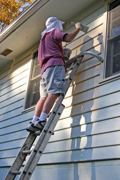 Man Balances On Ladder While Painting a House Exterior