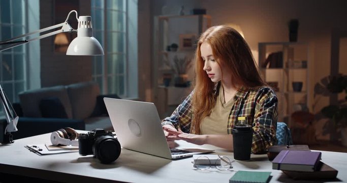 Cute caucasian girl concentrating on work at desk, using laptop to prepare for school or university exam, young freelancing manager working on a project 4k footage