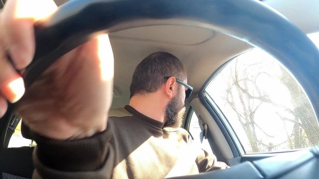 Adult man with sunglasses in car driving backwards from backyard to the road, wide angle view through the steering wheel