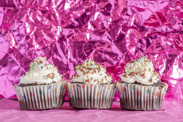 Delicious homemade cupcakes on a pink crumpled foil background. Holiday food