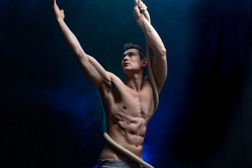 Muscular male circus artist with Cord Lisse on black an smoked background