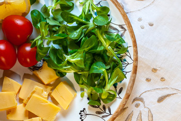 A plate with cheese cubes, cherry tomatoes and spinach leaves on provance authentic white tablecloth, close-up, top view