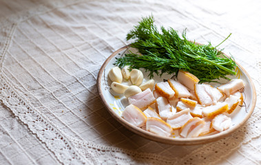 Ceramic plate with salo, green fennel and garlik on white rustic tablecloth