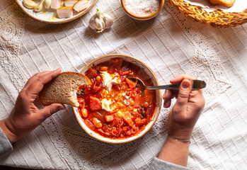 Woman's hands and Ukrainian borsch - well served with cream, garlic, salo, on white rustic tablecloth