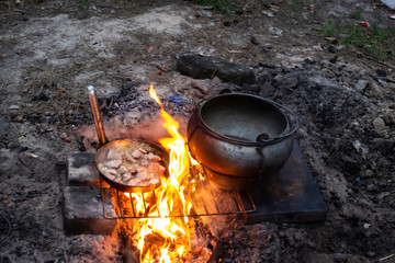 Field kitchen in the forest. Water boils and cooking food. Boiling pot  and frying pan above the fire, tourist meal cooking on fire