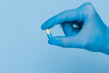 A hand in a blue medical glove holds one pill on a blue background. Disease Prevention Treatment