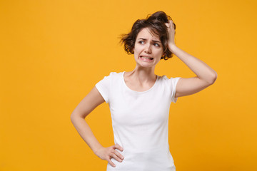 Preoccupied young brunette woman girl in white t-shirt posing isolated on yellow orange wall background studio portrait. People lifestyle concept. Mock up copy space. Put hand on head, looking aside.