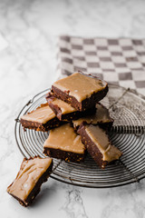 Group of stacked pieces of homemade chocolate caramel fudge cooling on a vintage rack on marble and a grey blocked dishcloth