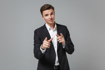 Smiling young business man in classic black suit shirt posing isolated on grey background in studio. Achievement career wealth business concept. Mock up copy space. Pointing index fingers on camera.