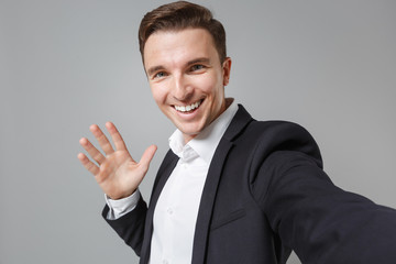 Close up of cheerful young business man in black suit shirt isolated on grey background. Achievement career wealth business concept. Mock up copy space. Doing selfie shot on mobile phone showing palm.