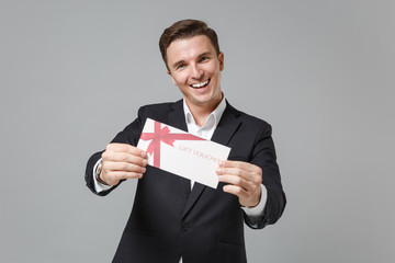 Cheerful young business man in classic black suit shirt posing isolated on grey wall background...