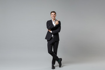Fototapeta na wymiar Smiling young business man in classic black suit shirt posing isolated on grey background studio portrait. Achievement career wealth business concept. Mock up copy space. Pointing index finger up.