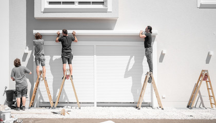 vier Handwerker hängen eine Markise an den Halterungen an der Hauswand ein