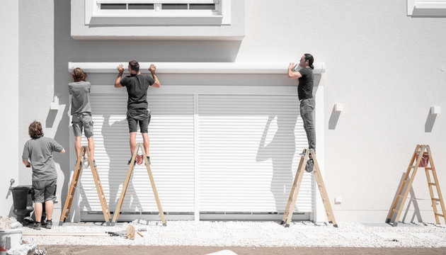 vier Handwerker hängen eine Markise an den Halterungen an der Hauswand ein