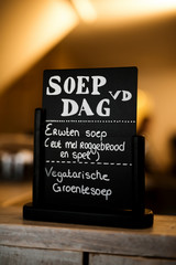 Dutch black sign with text soup of the day. Pea soup with rye bread and bacon and vegetarian vegetable soup. Erwtensoep met roggebrood en spek. Vegetarische groentesoep