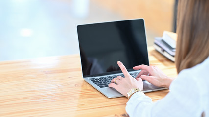 Cropped image of beautiful woman working as secretary typing on computer laptop while sitting at the wooden working desk over comfortable workplace as background.