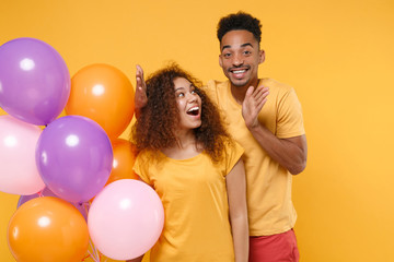 Excited young friends couple african american guy girl in casual clothes isolated on yellow orange background. Birthday holiday party people emotions concept. Celebrating hold colorful air balloons.
