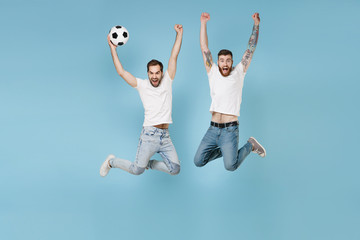 Fototapeta na wymiar Screaming young men guys friends in white t-shirt isolated on pastel blue background. Sport leisure concept. Cheer up support favorite team with soccer ball jumping rising hands doing winner gesture.