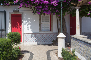 Lissabon, Portugal: Garten und Fassade mit typischen Fliesen, roter Tür  umrahmt von blühender lila Bougainvillea