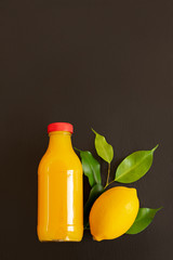 Fresh ripe lemons and a bottle with juice on a dark stone background. Top view with copy space.