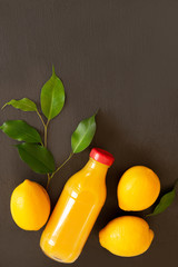 Fresh ripe lemons and a bottle with juice on a dark stone background. Top view with copy space.