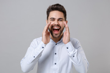 Crazy young unshaven business man in light shirt posing isolated on grey background in studio. Achievement career wealth business concept. Mock up copy space. Screaming with hands gesture near mouth.