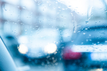 Water drops on a windscreen of a car on a rainy day. View from inside the car, blurred cars and city around,