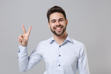 Cheerful young unshaven business man in light shirt posing isolated on grey wall background studio portrait. Achievement career wealth business concept. Mock up copy space. Showing victory sign.