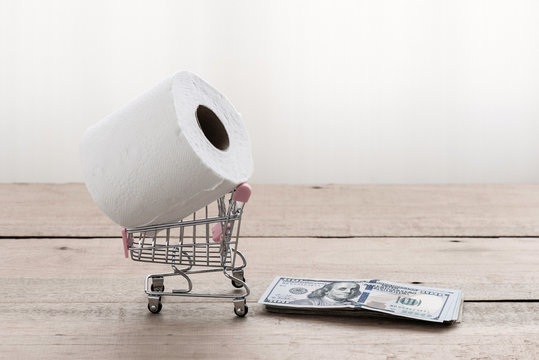 Tissue or toilet paper on shopping cart with cash dollar bills stck on wooden table. Concept of hoard supply due to covid-19 effect that rare item in some country