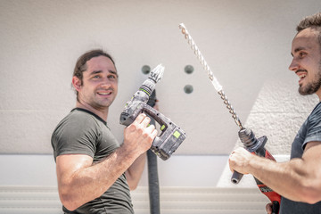 zwei freundliche Handwerker bohren mit der Bohrmaschine in die Hauswand um später eine Markise zu...