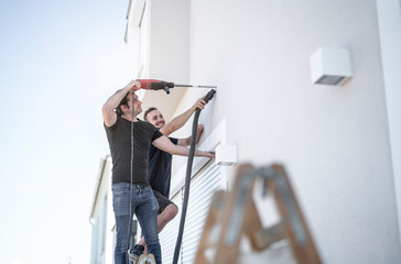 zwei freundliche Handwerker bohren mit der Bohrmaschine in die Hauswand um später eine Markise zu...