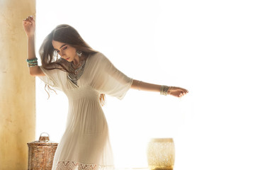 Beautiful girl in white dress and stylish jewelry inside room middle eastern interior