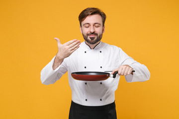 Smiling young bearded male chef cook or baker man in white uniform isolated on yellow background....