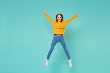 Obraz premium Funny young redhead woman girl in yellow knitted sweater posing isolated on blue turquoise background studio portrait. People lifestyle concept. Mock up copy space. Jumping spreading hands and legs.