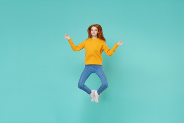 Fototapeta na wymiar Young redhead woman girl in yellow sweater posing isolated on blue turquoise background in studio. People lifestyle concept. Mock up copy space. Jumping hold hands in yoga gesture relaxing meditating.