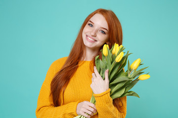 Smiling young redhead woman girl in yellow knitted sweater posing isolated on blue turquoise background studio portrait. People lifestyle concept. Mock up copy space. Hold bouquet of yellow tulips.