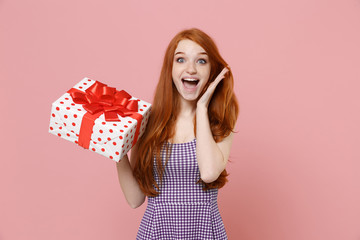 Excited redhead girl in plaid dress isolated on pastel pink background. Valentine's Day, Women's Day, birthday, holiday concept. Mock up copy space. Hold white red present box with gift ribbon bow.