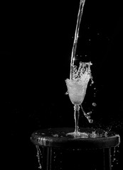 Plano detalle de una copa de cristal llenándose de agua, con gotas de agua salpicando 