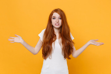 Perplexed young redhead woman girl in white blank empty t-shirt posing isolated on yellow background studio portrait. People sincere emotions lifestyle concept. Mock up copy space. Spreading hands.